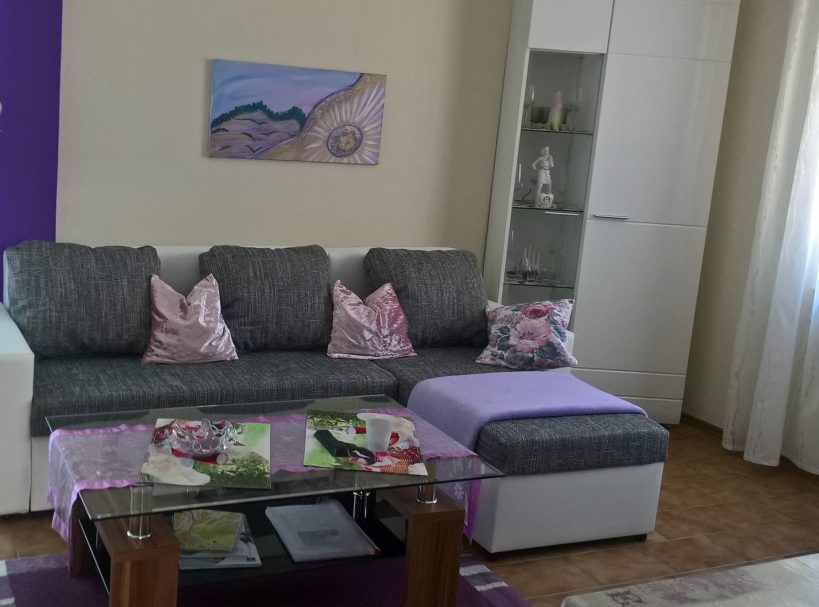 Ferienwohnung Romantic Moderne Wohnzimmercouch mit Kissen, Glastisch und dekorativen Elementen.